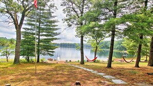 Ein Campingplatz am See mit Bäumen, einer Hängematte und einer Fahnenstange.