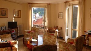 Uma sala de estar com móveis estampados em florais, uma televisão e um espaço de jantar com mesa e cadeiras.