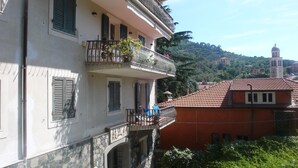 Um edifício com varanda, fachada de pedra e vista para uma colina com uma torre.