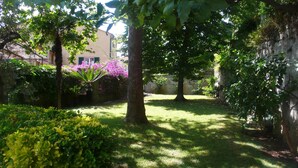 Um jardim exuberante com árvores frondosas, gramado bem cuidado e plantas floridas.