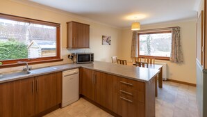 A kitchen with wooden cabinets, a dishwasher, a microwave, and a dining area with chairs. - Pet-friendly holiday home in the quiet hamlet of Drumguish (Kingussie)