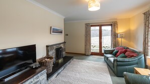 A living room with a flat-screen TV, fireplace, sofa, and a view through a glass door. - Pet-friendly holiday home in the quiet hamlet of Drumguish (Kingussie)