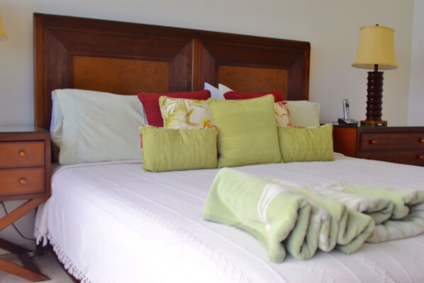 A neatly made bed with a white comforter, green and red pillows, and a folded green towel.