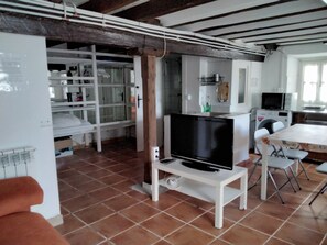 Eine kleine Küche mit Fernseher auf einem Schrank, einem Esstisch mit Stühlen und einem weißen Schrank mit Regalen.
