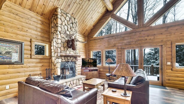 Ein Holzblockhaus-Interieur mit Kamin aus Stein, einer Ledersofa und Holzboden.