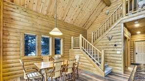 Ein Holzblockhaus-Innenraum mit Essbereich, einer Holztreppe und großen Fenstern.