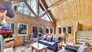 Ein rustikales Blockhaus-Interieur mit großem Fenster, einem Ledersofa, einem Holztisch und einem Teppich.
