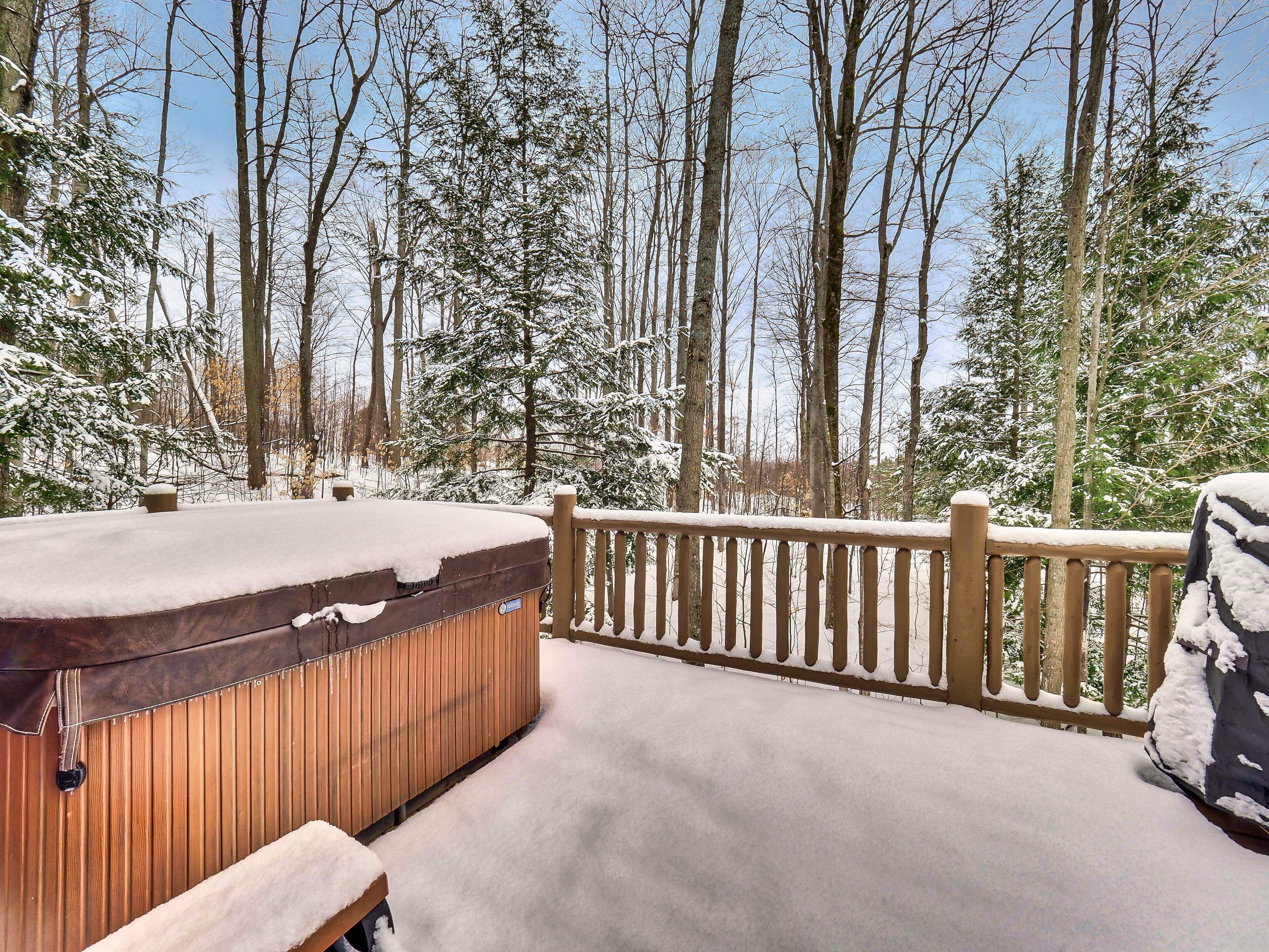 A hot tub on a wooden deck with snow-covered trees in the background.