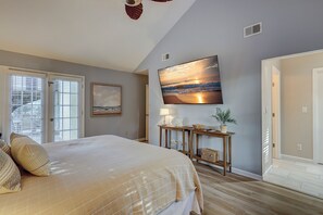 Une chambre à coucher comprenant un lit, un tableau, une console ornée d’objets décoratifs et un grand téléviseur fixé au mur.