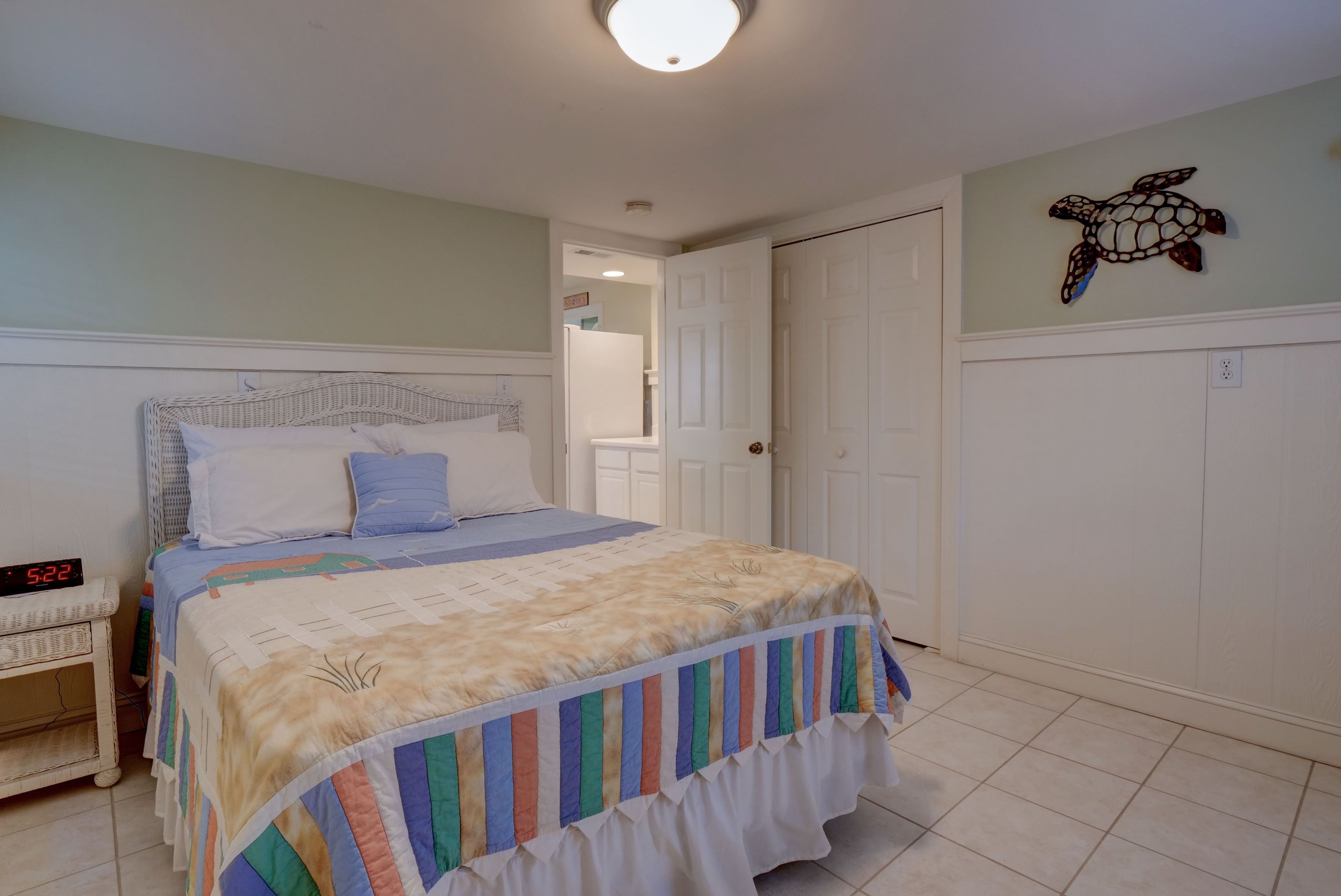 A neatly arranged bedroom with a bed, a nightstand, a wall-mounted turtle decoration, and a door leading to another room.
