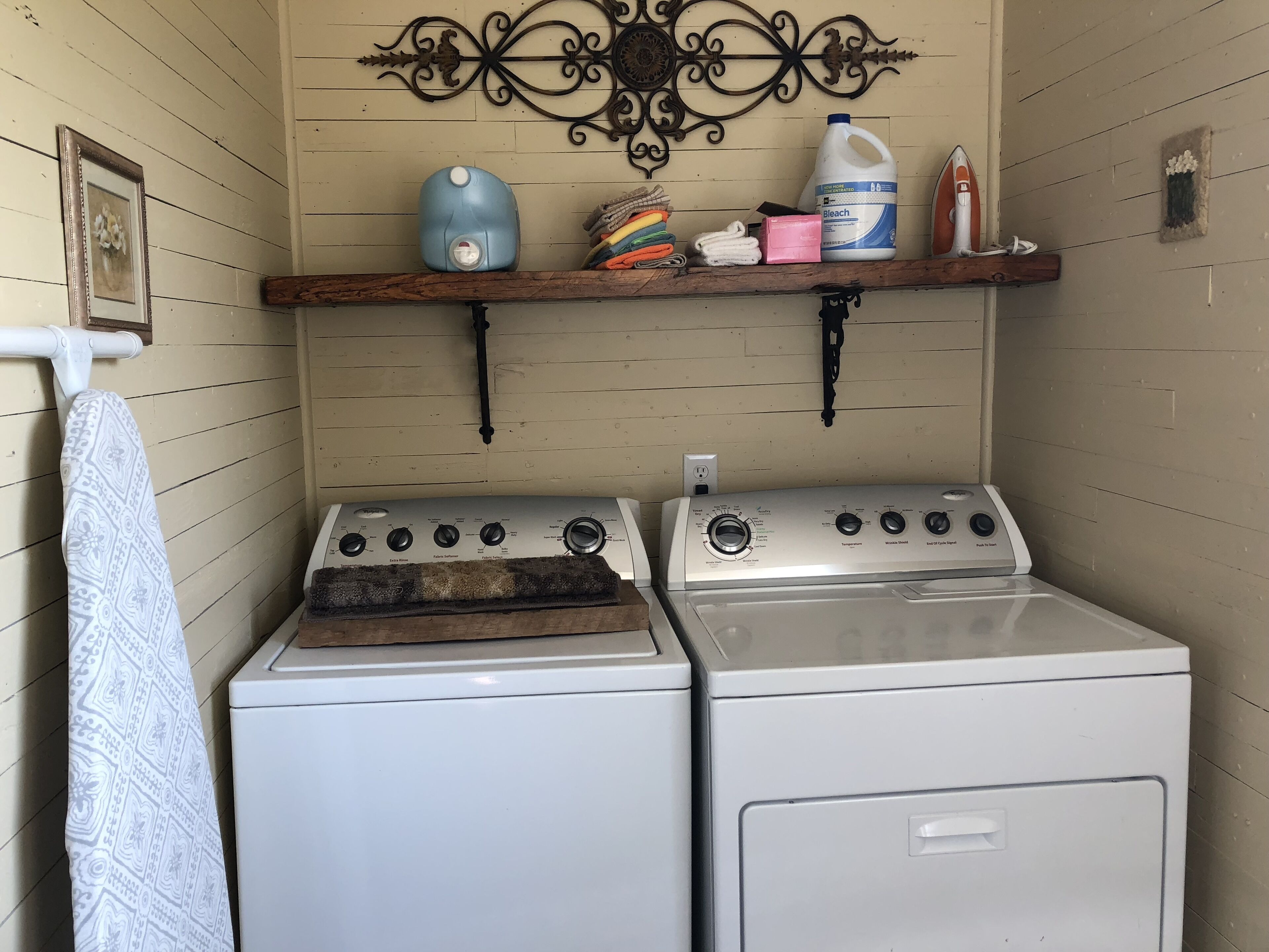 A laundry area with a washing machine and dryer, a shelf with cleaning supplies, and a decorative wall piece.