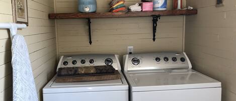 A laundry area with a washing machine and dryer, a shelf with cleaning supplies, and a decorative wall piece.