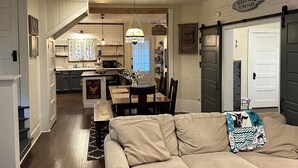 A spacious living room with a large beige sectional sofa, a dining area with a wooden table and chairs, and a kitchen with white cabinets and a hanging light fixture. - Country Cottage Hideaway near Lynchburg  (Fayetteville)