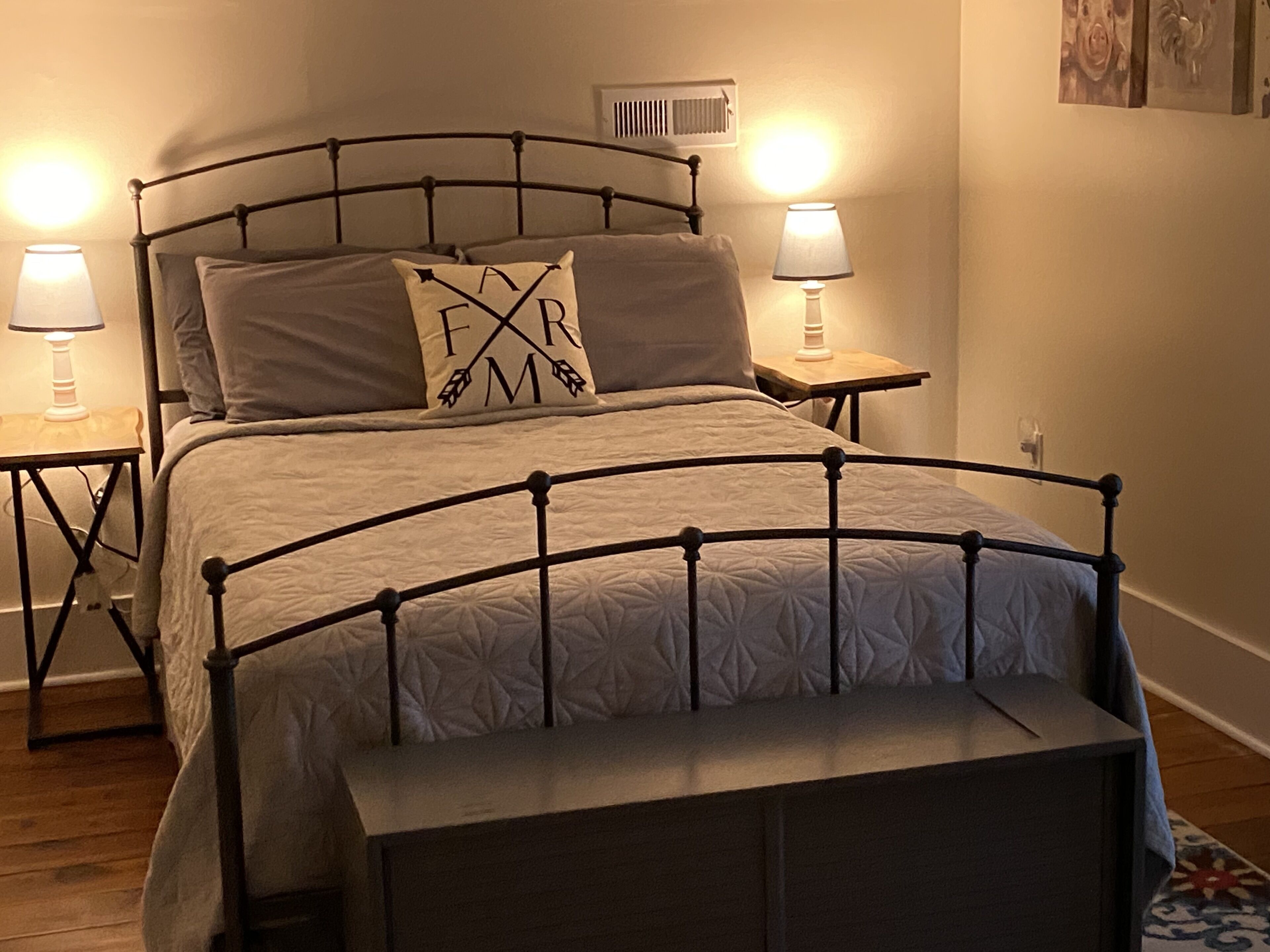 A bed with a metal frame, two bedside lamps, and a pillow with 'FARM' embroidered on it.