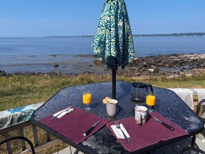 A table set for breakfast with a view of the water, a kettle, and a coffee pot.
