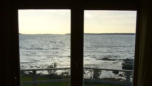 A room with a large sliding glass door leading to a wooden deck overlooking a body of water. - Private Oceanfront Cottage, Private Sand Beach -Lighthouse one mile away (Permaquid Point)