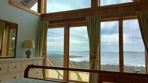 A bedroom with a large bay window overlooking the sea, a bed, a dresser, and a lamp. - Private Oceanfront Cottage, Private Sand Beach -Lighthouse one mile away (Permaquid Point)