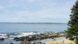 A deck with a glass table and two wicker chairs overlooking a rocky shoreline and ocean. - Private Oceanfront Cottage, Private Sand Beach -Lighthouse one mile away (Permaquid Point)