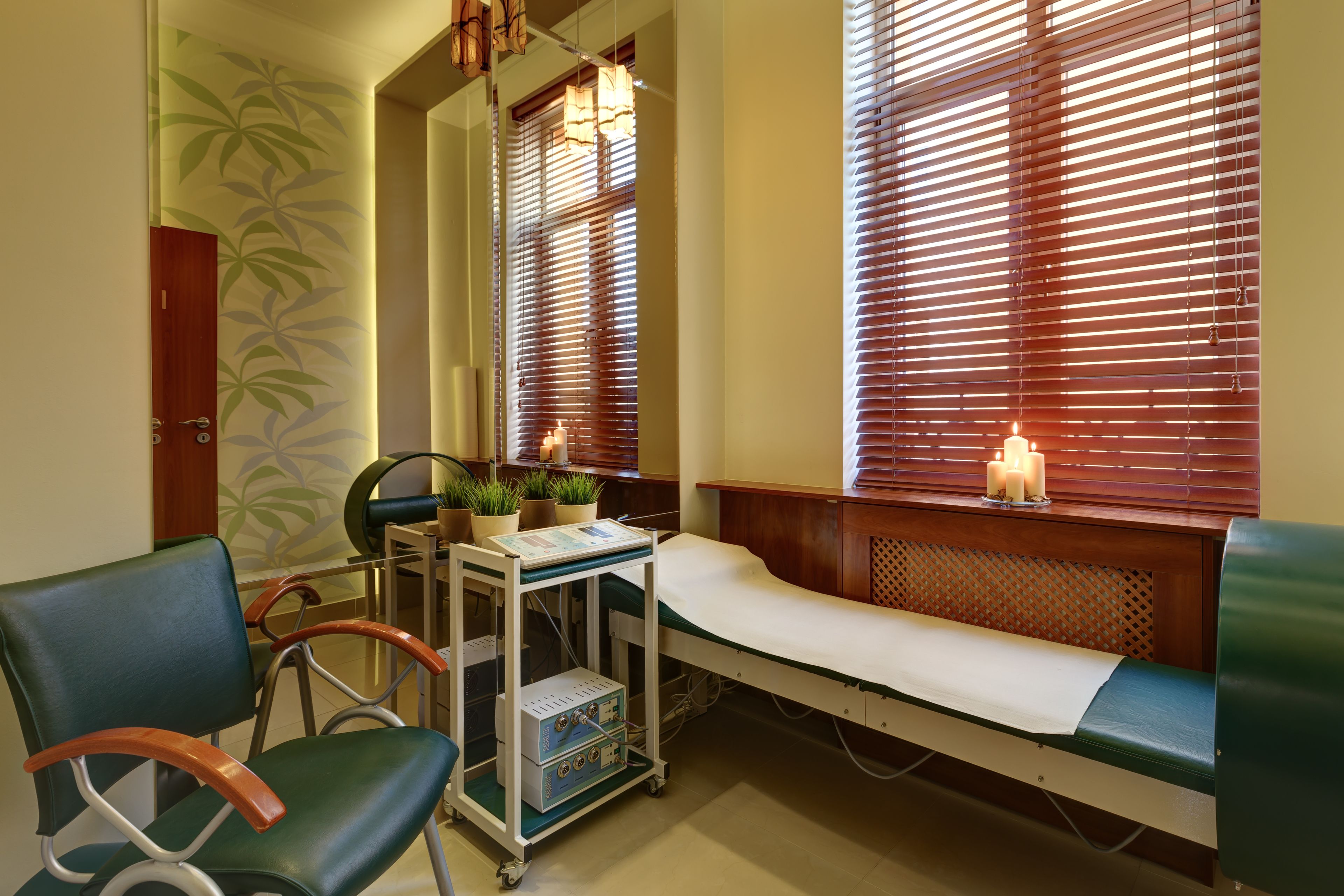 A medical examination room with a wooden bench, examination table, and a cart with medical equipment.