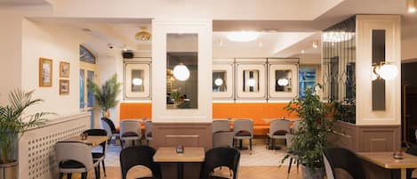 A restaurant with booths and tables, wooden flooring, and potted plants.
