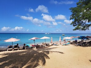 Une plage avec des transats et des parasols, un ciel dégagé et un bateau à l’horizon.