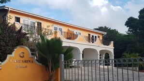 Un edificio con fachada amarilla, entrada protegida por un portón y un letrero que dice "CASUARINA Grande".
