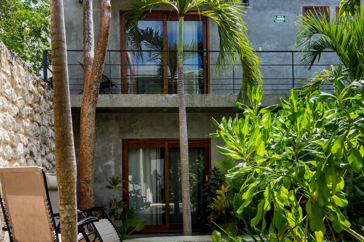 Un edificio de dos pisos con piscina, mobiliario exterior y abundante vegetación.