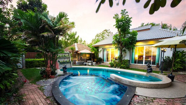 Un jacuzzi rodeado de un jardín con una casa al fondo.