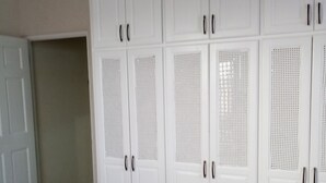 A room with a large white wardrobe with multiple doors and drawers, a bed with a polka dot bedspread, and a plain wall. - Sand Dollar Vacation Apartment Rental (Mangrove)
