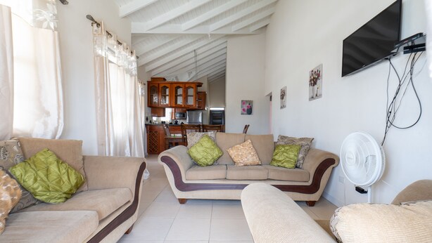 A living room with a sofa, a chair, a TV mounted on the wall, and a fan. - Sand Dollar Vacation Apartment Rental (Mangrove)