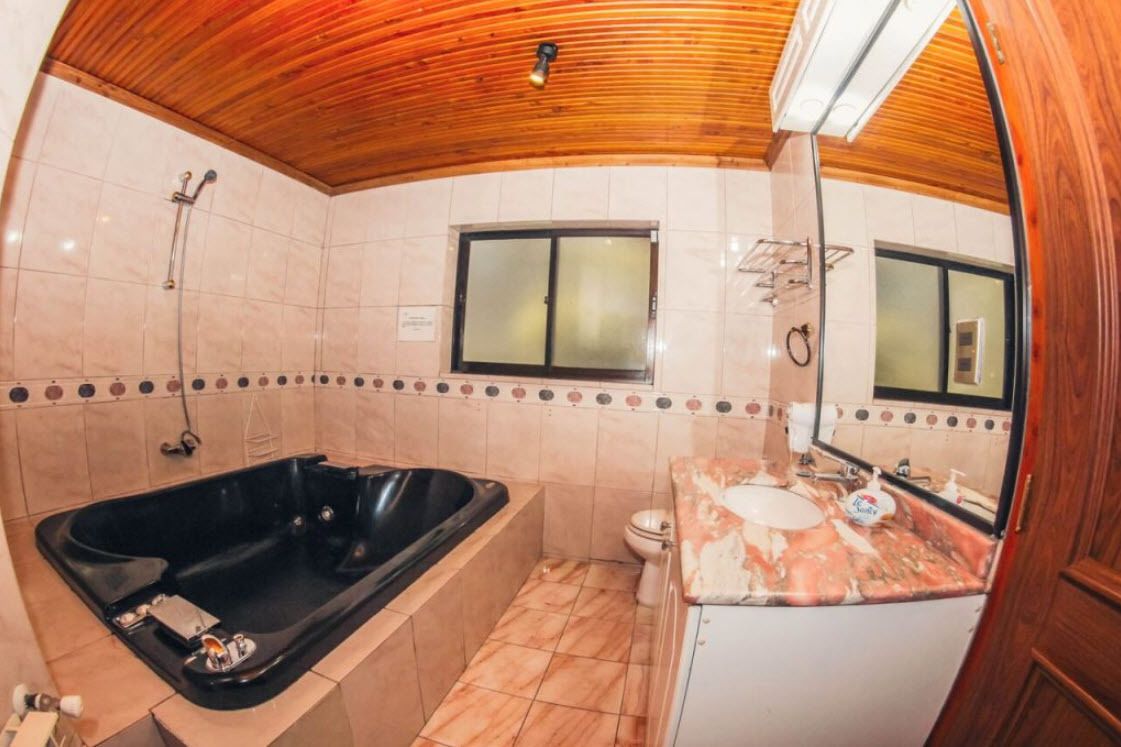 Un baño con techo de madera, una bañera negra, un inodoro y un lavabo con espejo.