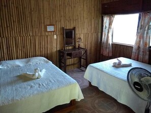 A room with two beds, a desk, a mirror, and a fan.