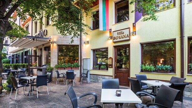 An outdoor patio area with tables and chairs, a sign for 'Villa Boyana', and potted plants. - Hotel Villa Boyana (Sofia)