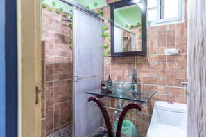 A bathroom with a glass sink, a white toilet, and a shower area with a door. - Modern Bilton Apartment (Montego Bay)