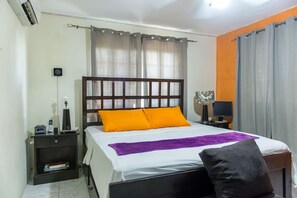 A neatly made bed with a wooden headboard, a bedside table with a lamp, and a small shelf with books. - Modern Bilton Apartment (Montego Bay)