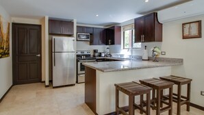 Une cuisine moderne dotée d’un îlot central, de meubles en bois foncé, d’appareils électroménagers en acier inoxydable et d’un sol carrelé.