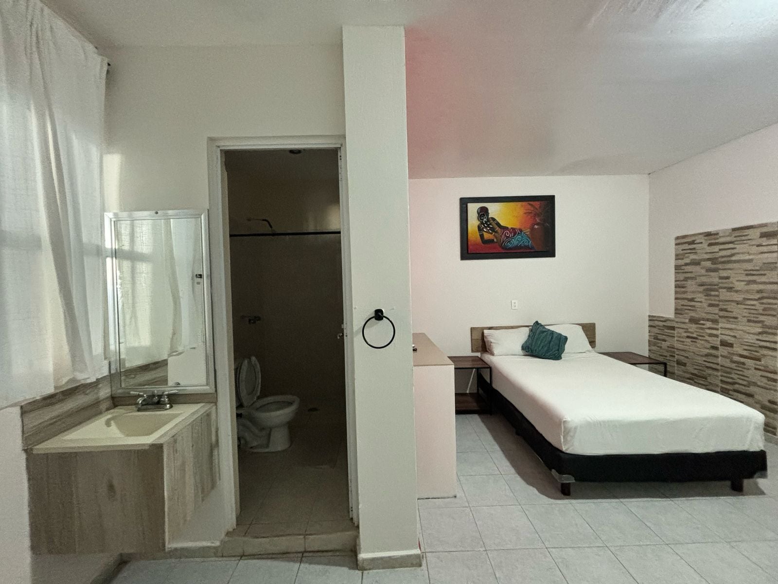 Habitació amb llit, una taula de nit, vàter i zona de dutxa.