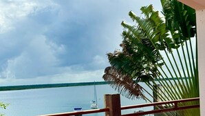 Un balcón con un banco acolchado blanco, una mesa de madera y vistas a una masa de agua tranquila con barcos.