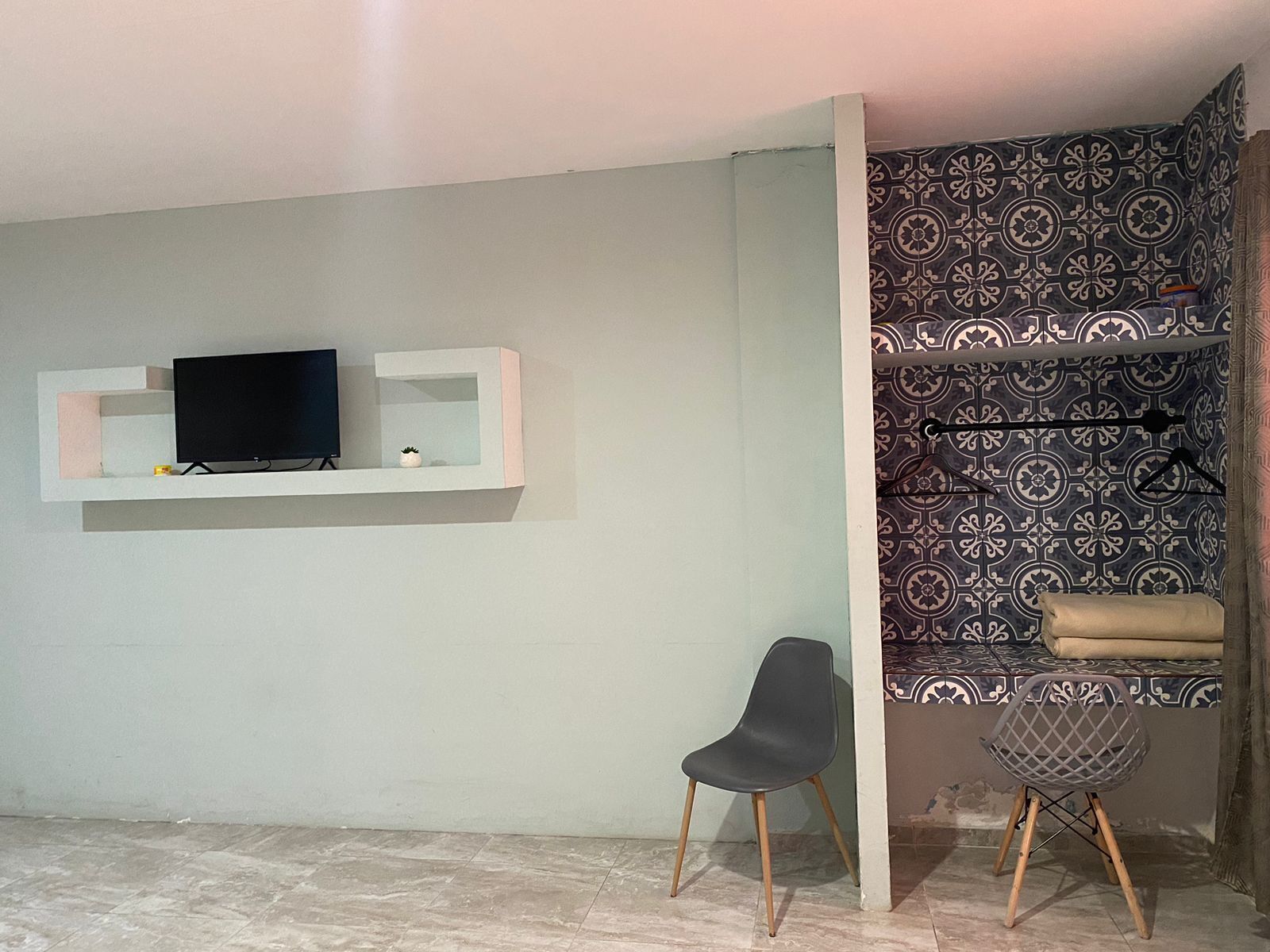 A living room with a TV on a white shelf, a black chair, and patterned wallpaper.