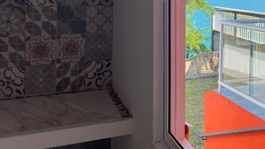 Un baño con salpicadero de azulejos y una ventana con vistas a un balcón sobre el mar.