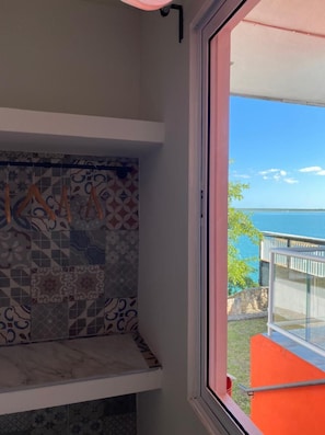 A bathroom with a tiled backsplash and a window overlooking a balcony with a view of the sea. - Hotel Awazul Bacalar (Bacalar)