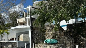 Zona de piscina con sillones reclinables azules, un muro de piedra y un edificio al fondo.