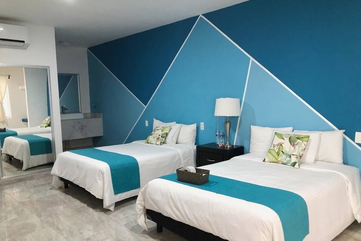 A hotel room with two beds, a nightstand, a lamp, and a large mirror.