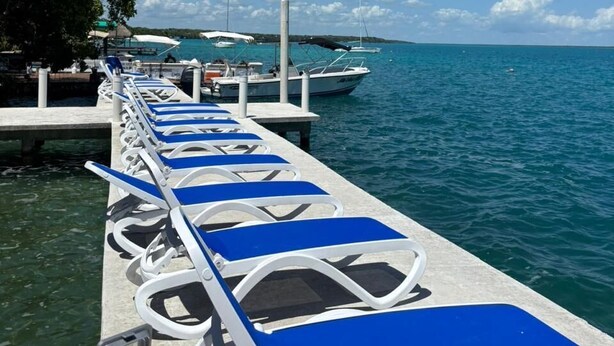 Un muelle con sillones de descanso, un barco amarrado y un cielo azul despejado.