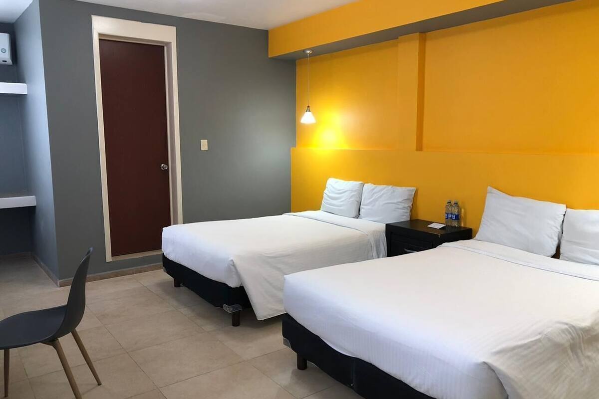 A hotel room with two beds, a desk, a chair, and a door.