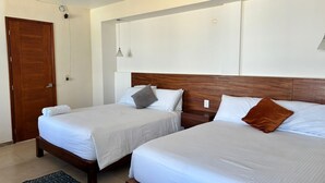 Habitación de hotel con dos camas individuales, una puerta de madera, una pared blanca, una lámpara en el techo y una alfombra pequeña.