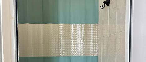 A bathroom with a shower curtain, a toilet, and a wall-mounted toilet paper holder.