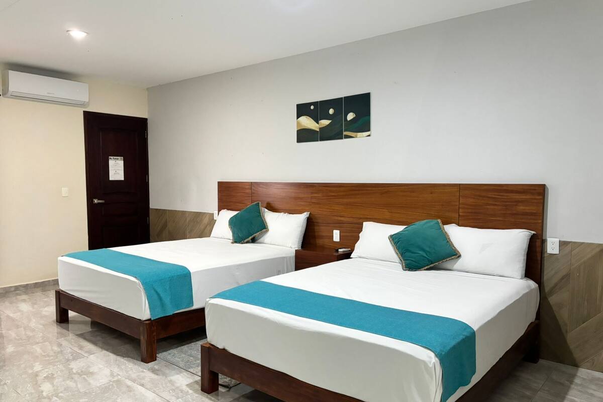 Two single beds with wooden headboards, white bedding, and teal throw pillows.