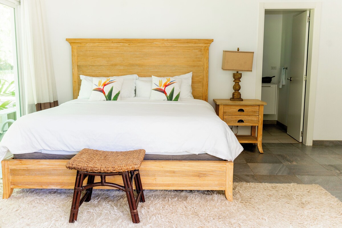 Een bed met een houten hoofdbord, wit beddengoed en decoratieve kussens.