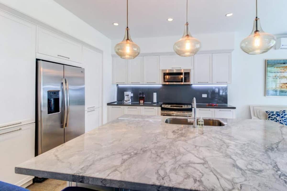 A modern kitchen with a marble island, stainless steel appliances, and pendant lighting.
